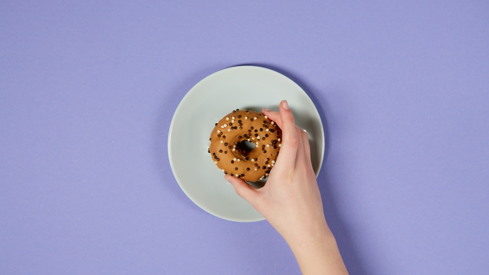 Hand reaching for a donut on a blue purple colored table linen