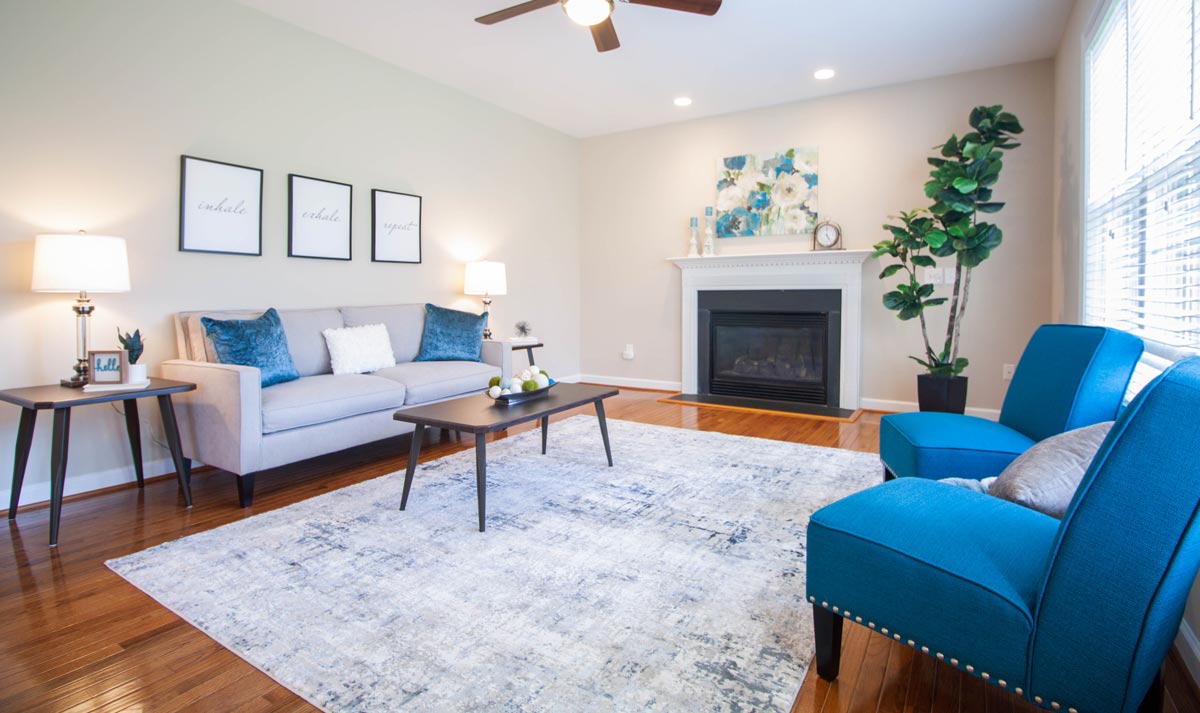 A vacant home staging of a contemporary living room with fireplace, blue accent chairs, grey loveseat, and other home staging essentials