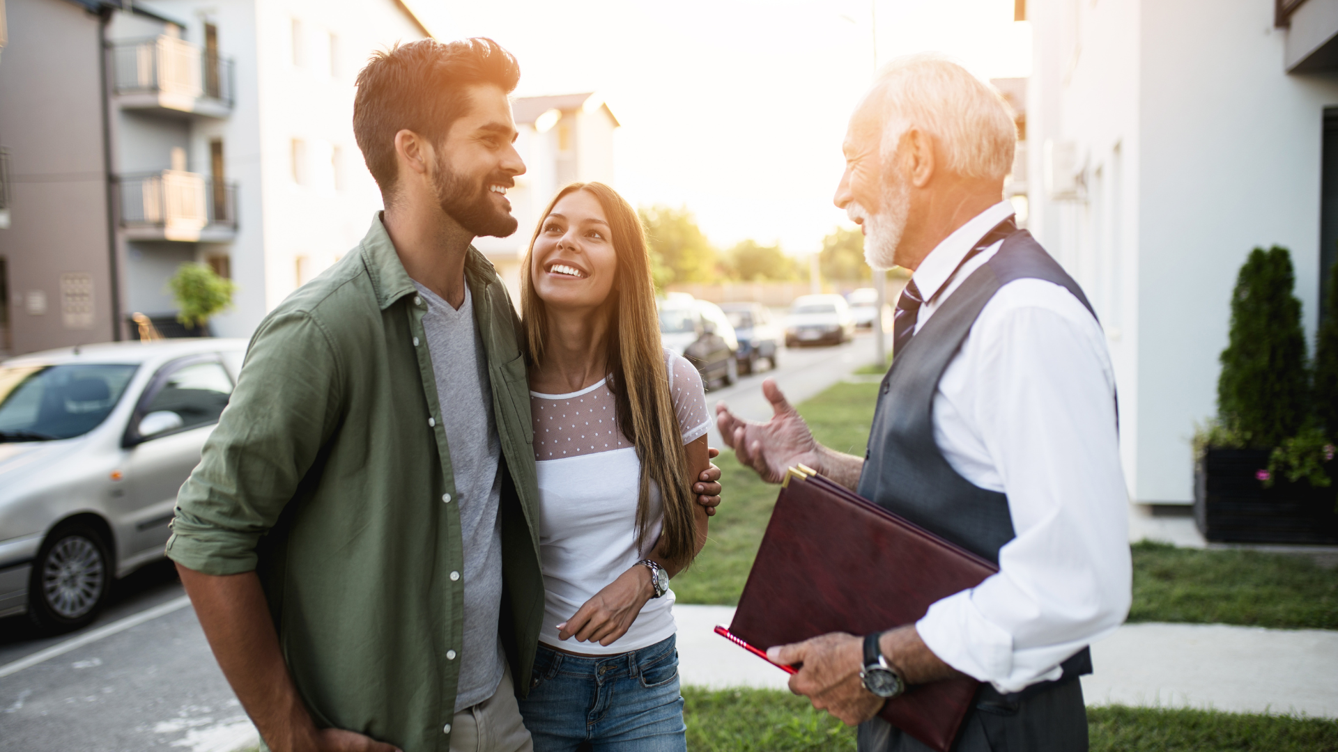 A couple speaking with a realtor while holding a brochure, discussing whether they should be buying a house in 2023.