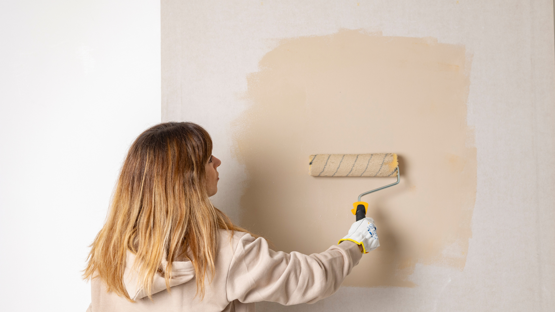 Home Improvement Projects - Woman using a paint roller to paint a wall in a neutral beige color