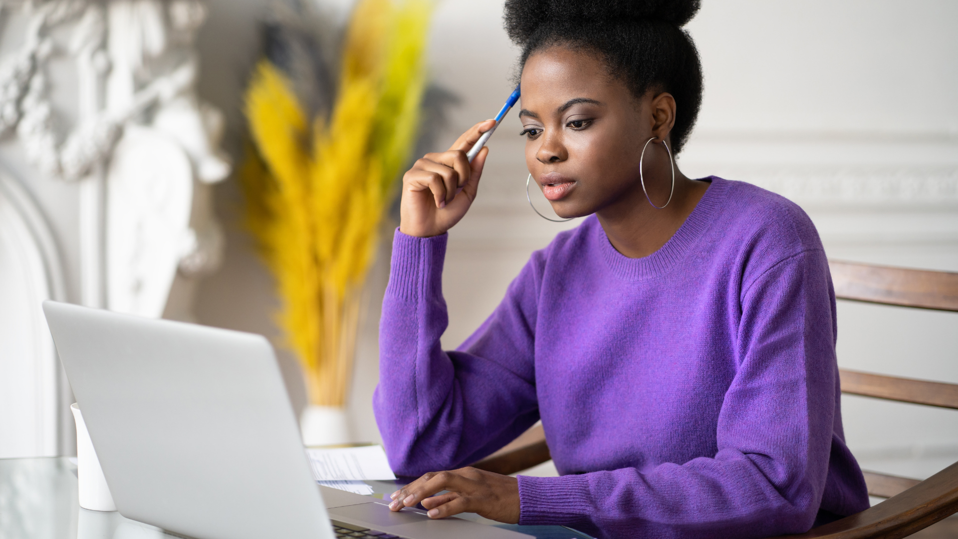 Woman in purple sweater reads online furniture reviews on white laptop