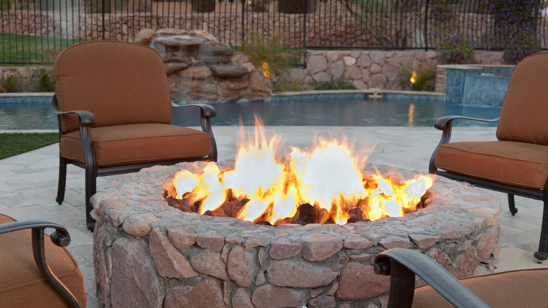 Real estate photos - backyard stone firepit by swimming pool with patio chairs